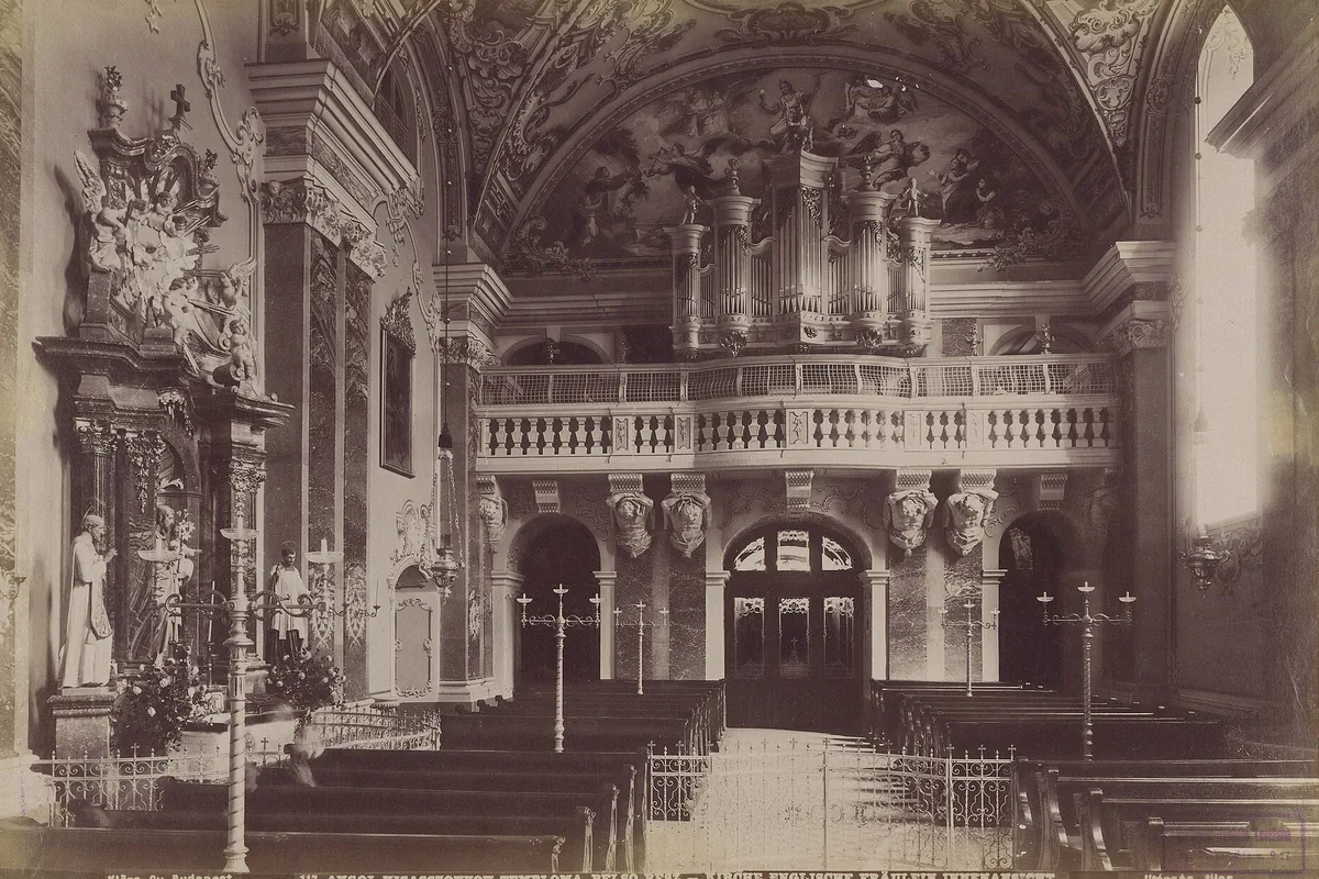 A sepia photograph of the church interior around 1892, with the organ gallery above a balustrade, an altar on the left and rows of pews in front