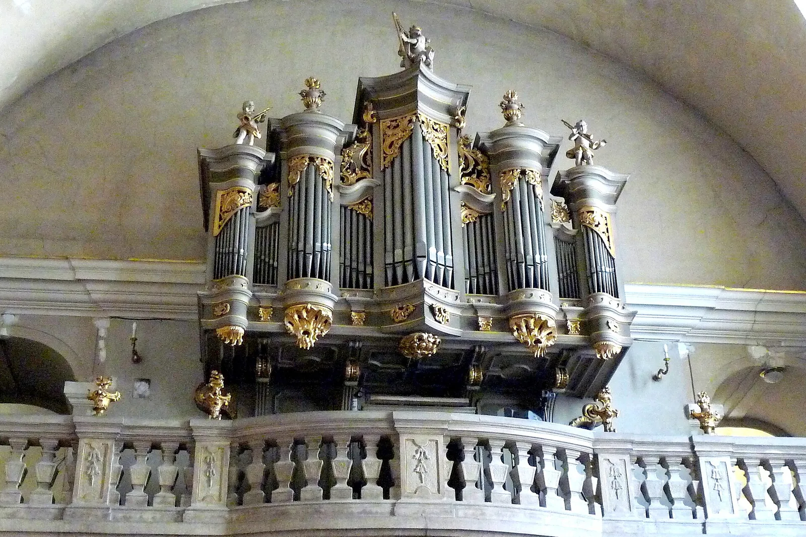 The organ in its gallery at the west end of the church, with silver pipes in a gilded case above a stone balustrade and a pale vaulted ceiling